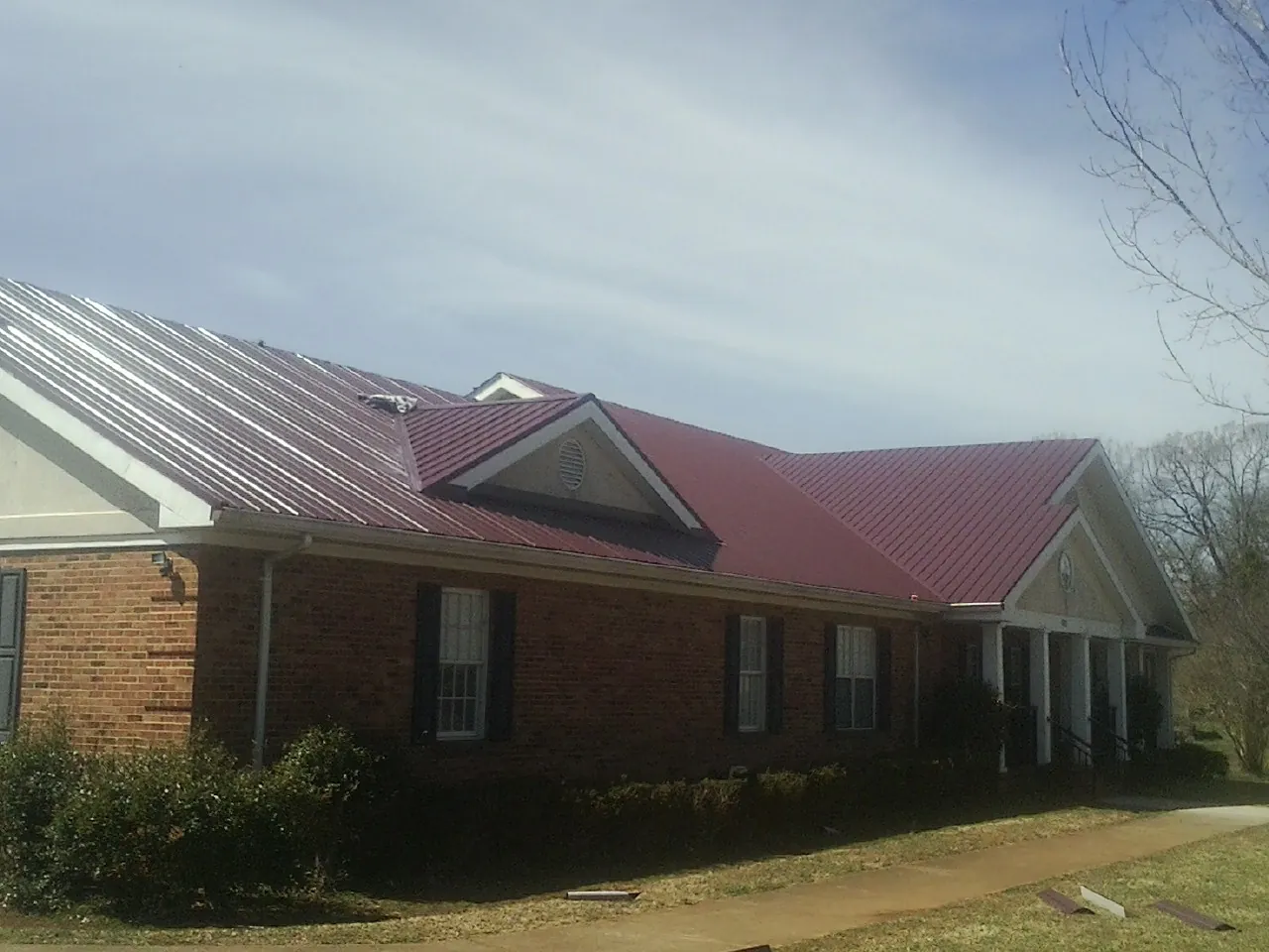 Red metal roof with gabled entries on a long brick building, from a Hail Damage Roof Repair job in Rantoul
