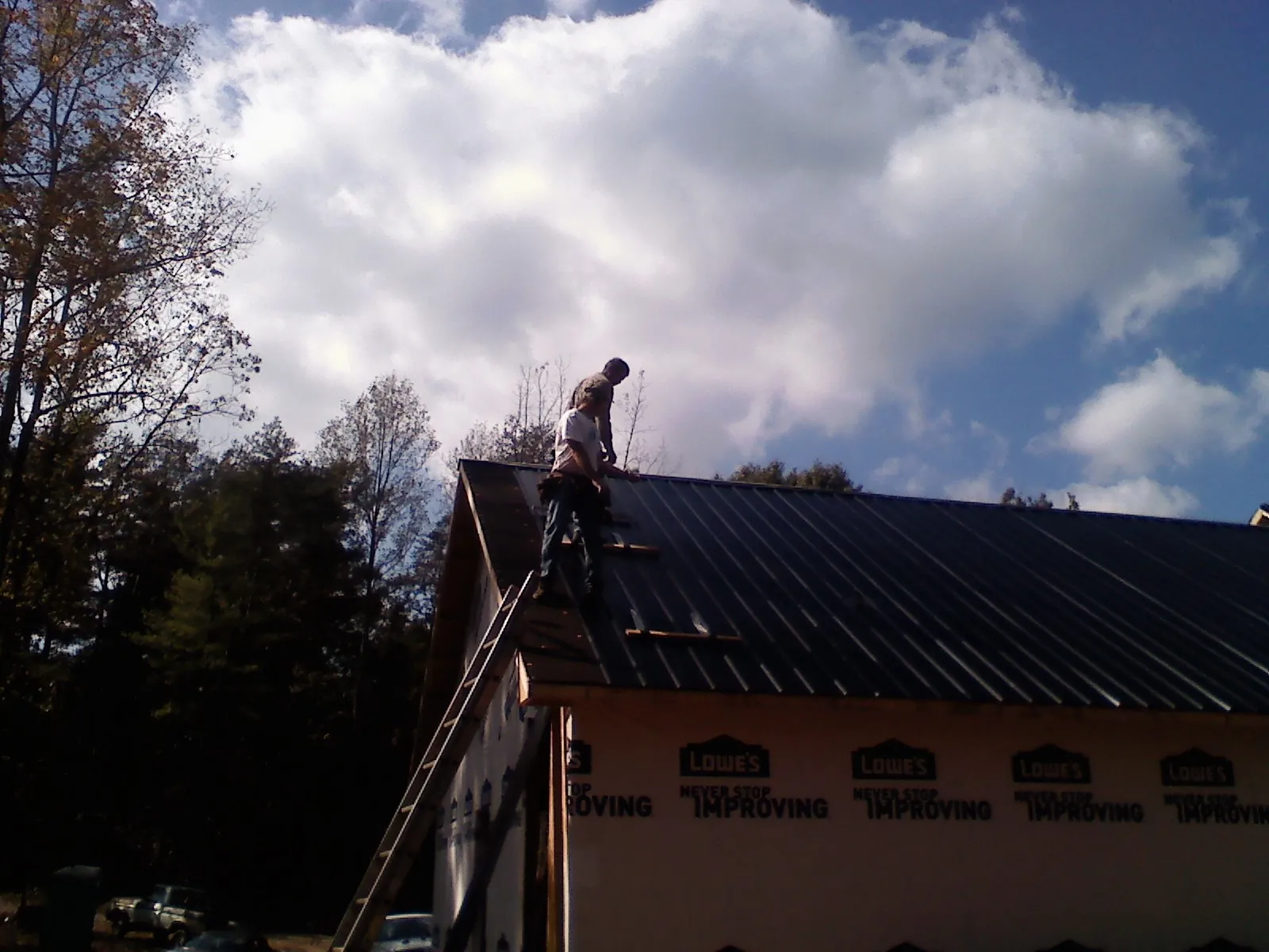 Roofer fastening dark metal panels high against a cloudy sky, from a Roof Inspection job in Rantoul