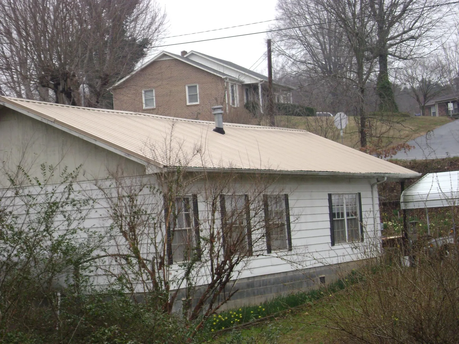 Tan metal roof on a white sided house set into a hillside — Commercial Roofing by Roofing Brothers in Rantoul